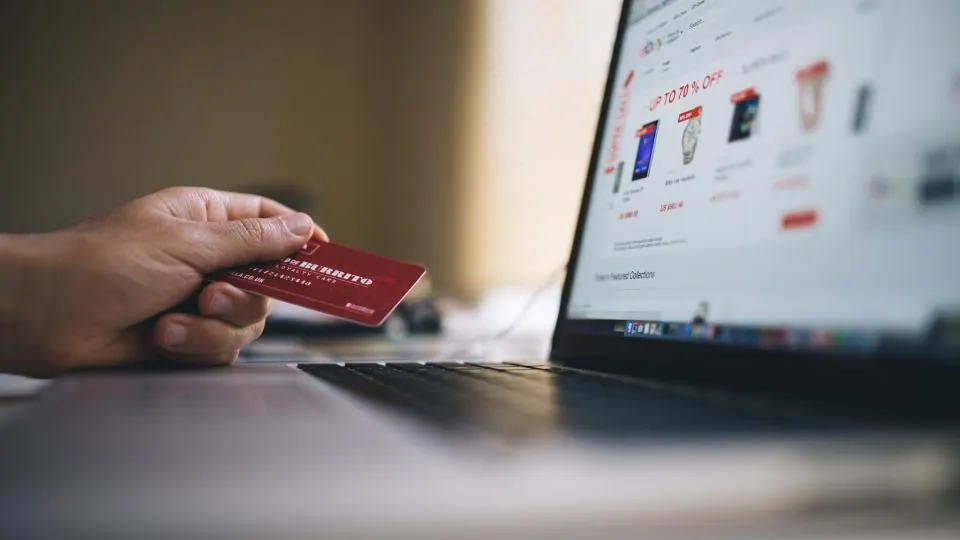 Persona pagando una compra en línea con tarjeta frente a un portátil